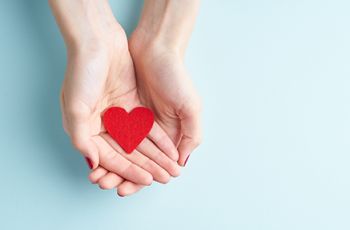 hands holding a red heart on a blue background